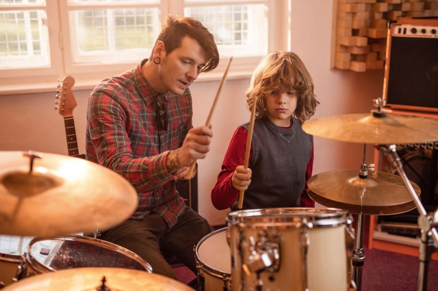 Young father showing his son how to play drums.